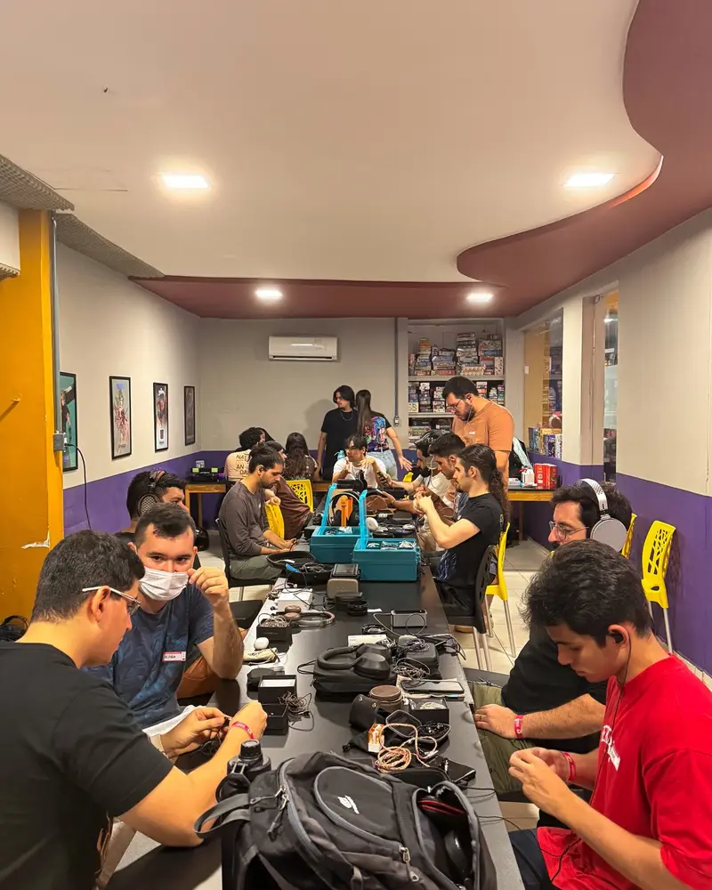 Mesa comprida com participantes ouvindo fones lado a lado